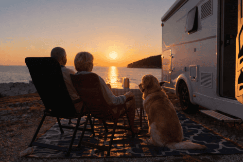 Twee ouderen genieten van een rustige camperplek aan zee bij zonsondergang, met hun hond en camper, perfect voor 60-plussers die willen ontspannen tijdens hun camperreis in Europa.